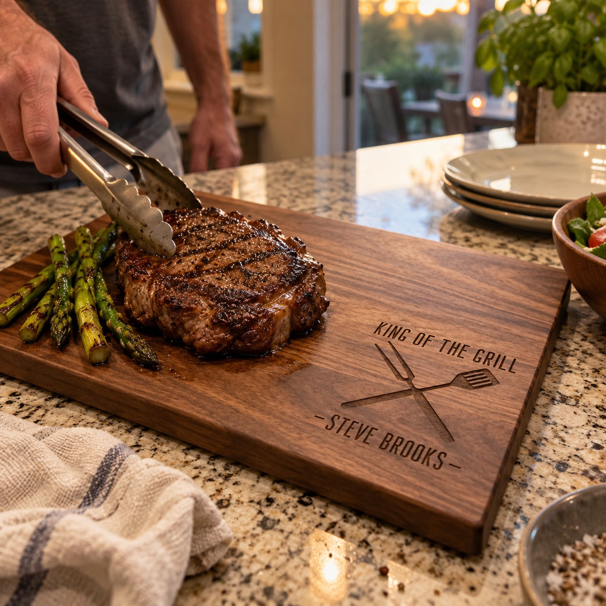 A man sets a grilled ribeye with tongs on a King of the Grill cutting board engraved STEVE BROOKS, a personalized gift for men that grill