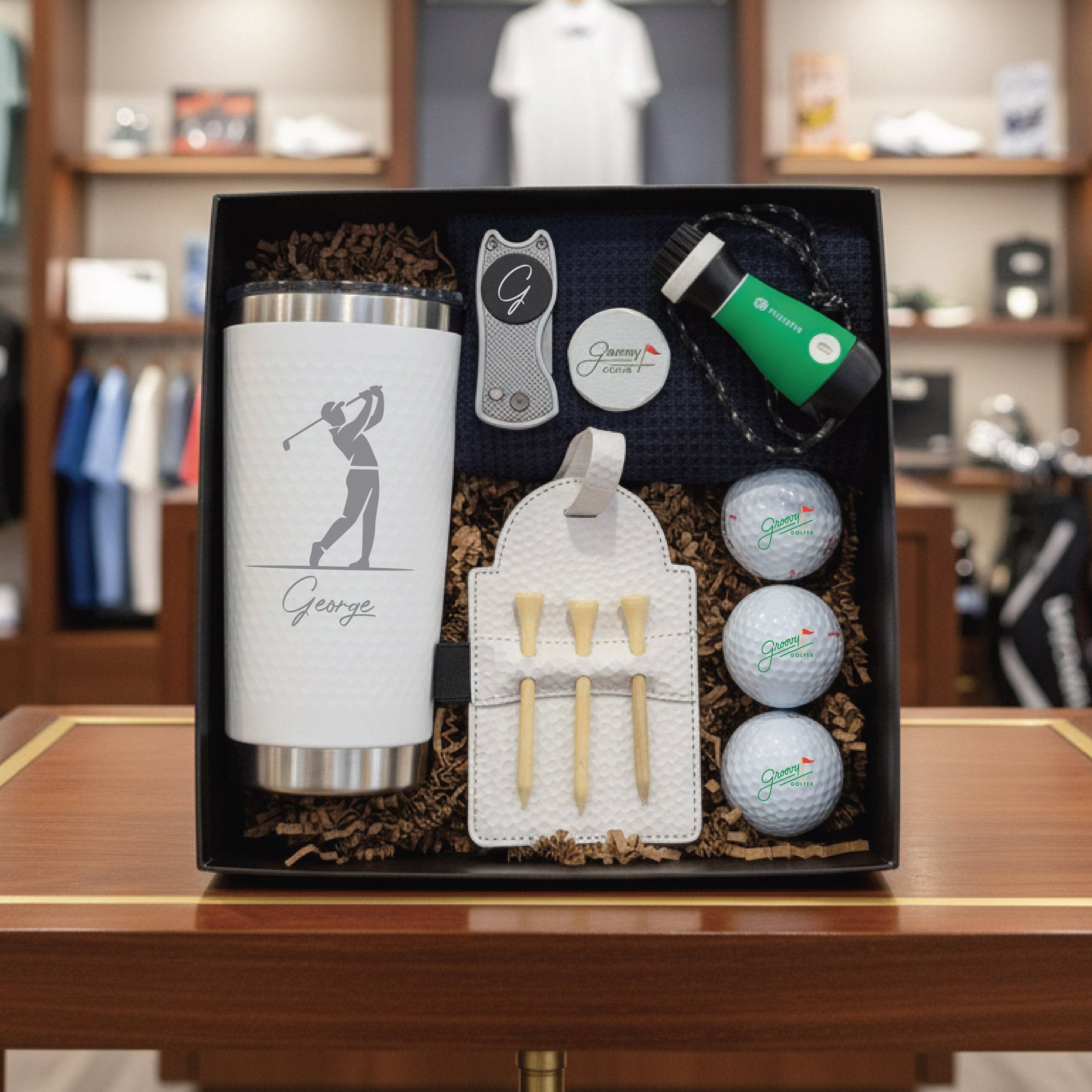 Golf-themed gift set with tumbler, golf balls, tees, and other items in a black box.