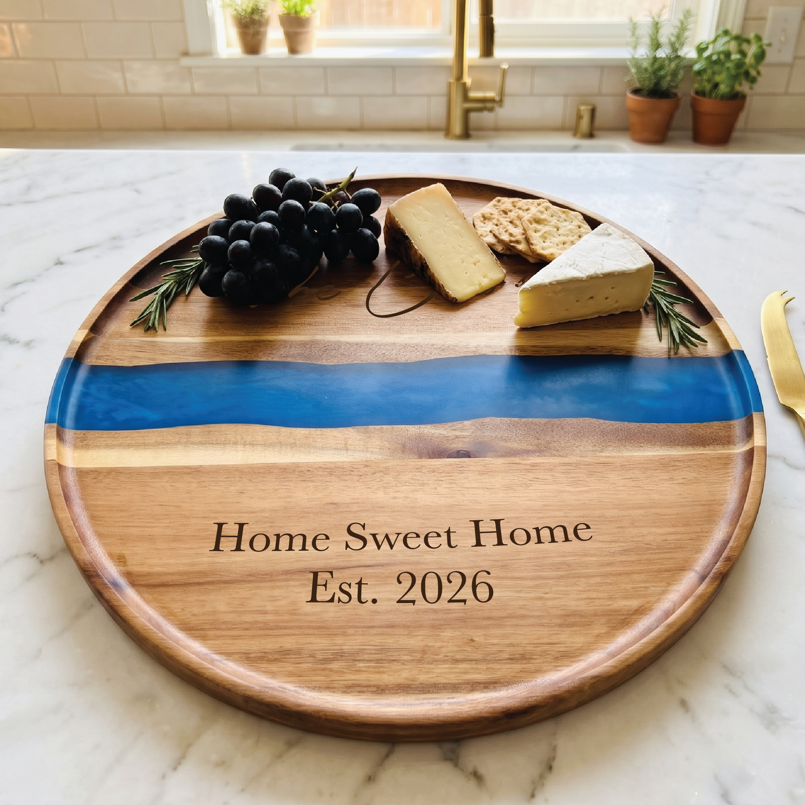 Custom round acacia board with a blue resin river holding grapes, cheese and crackers, engraved Home Sweet Home Est. 2026 below the river