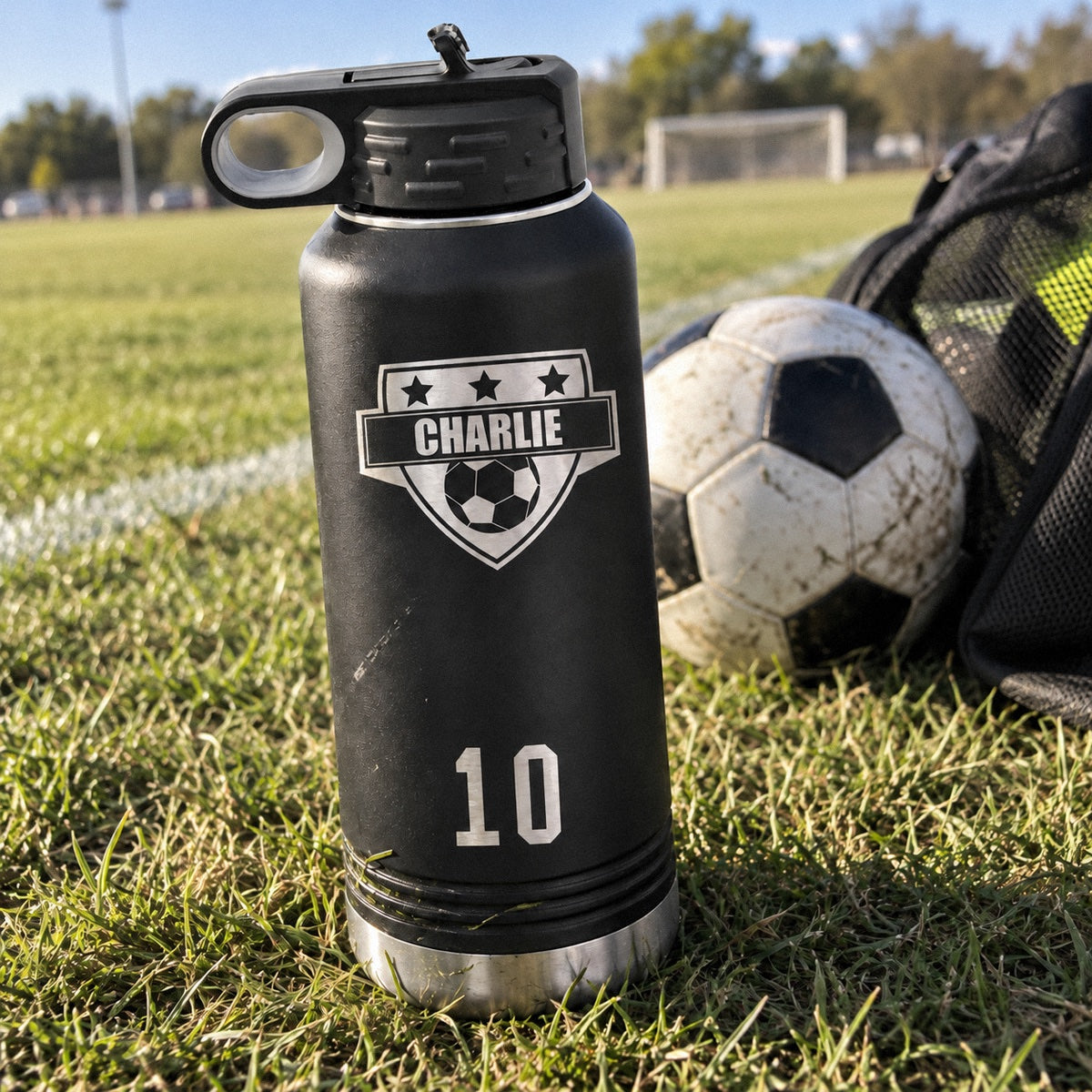 Kick and Sip personalized soccer water bottle with CHARLIE on a soccer crest and a big 10, a 32 oz black bottle on the field by a ball