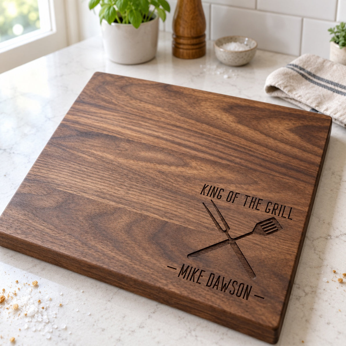 King of the Grill personalized cutting board in walnut with a crossed fork and spatula and the name MIKE DAWSON engraved, on a kitchen counter