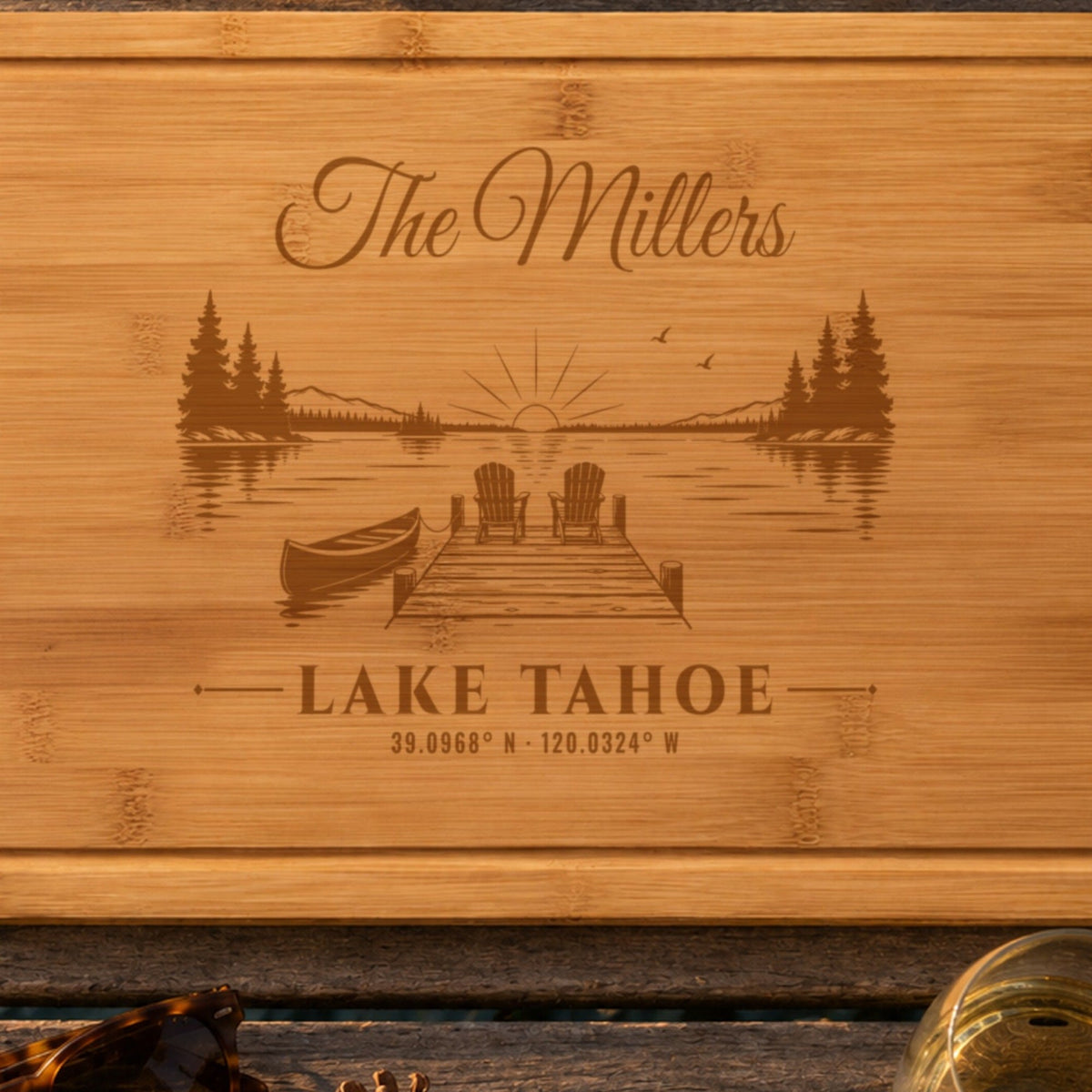 Close-up of the laser engraving on the lake house cutting board: The Millers in script, a dock with two Adirondack chairs and a canoe, and Lake Tahoe