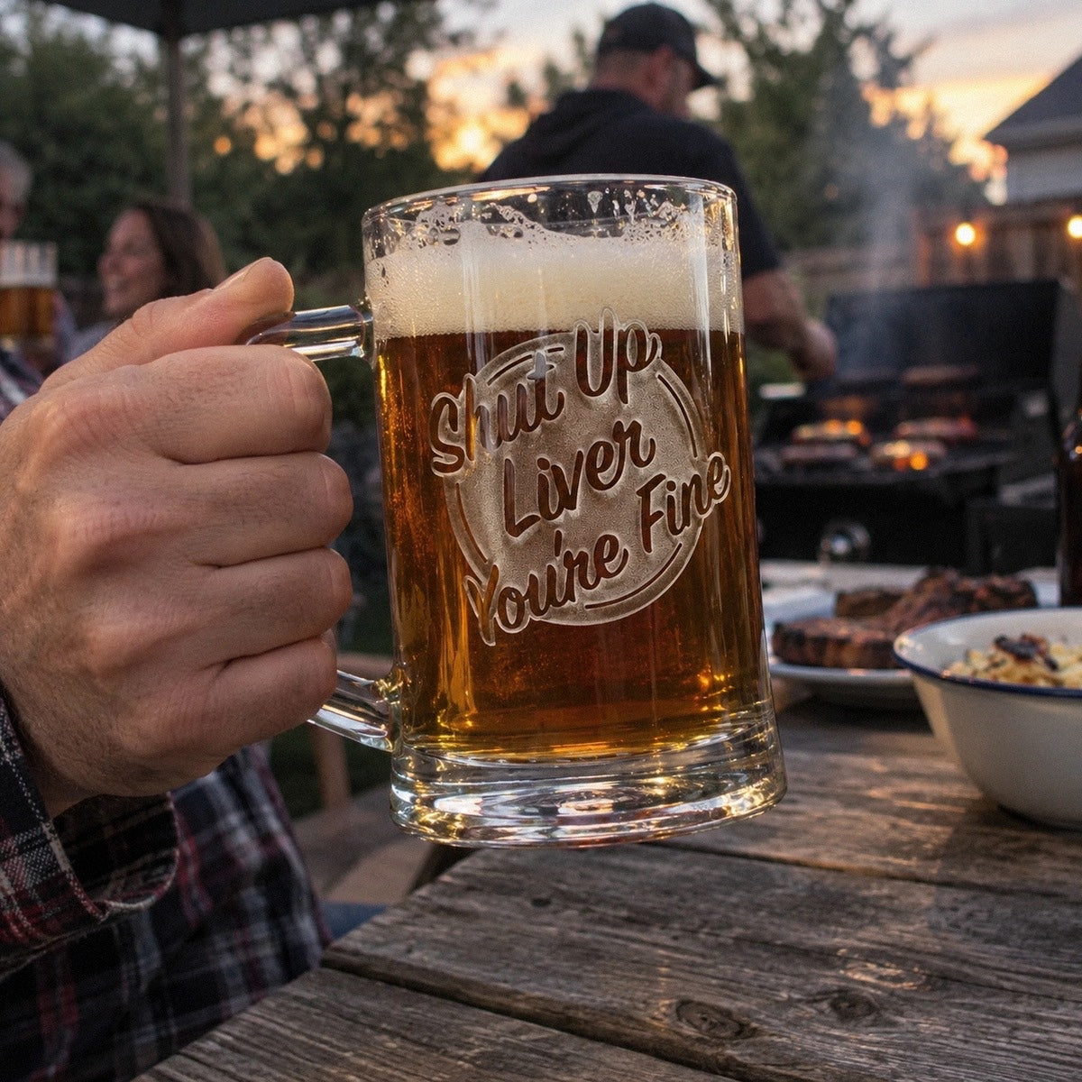 A man lifts his Shut Up Liver You're Fine funny beer mug at a backyard grill night, one of the novelty beer mugs that always gets a laugh