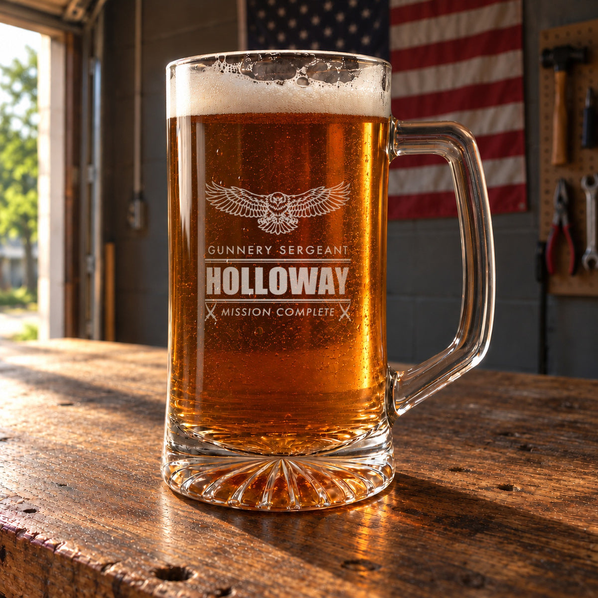 Marine retirement beer stein on a garage workbench with an American flag behind it, engraved with an eagle, Gunnery Sergeant and Holloway