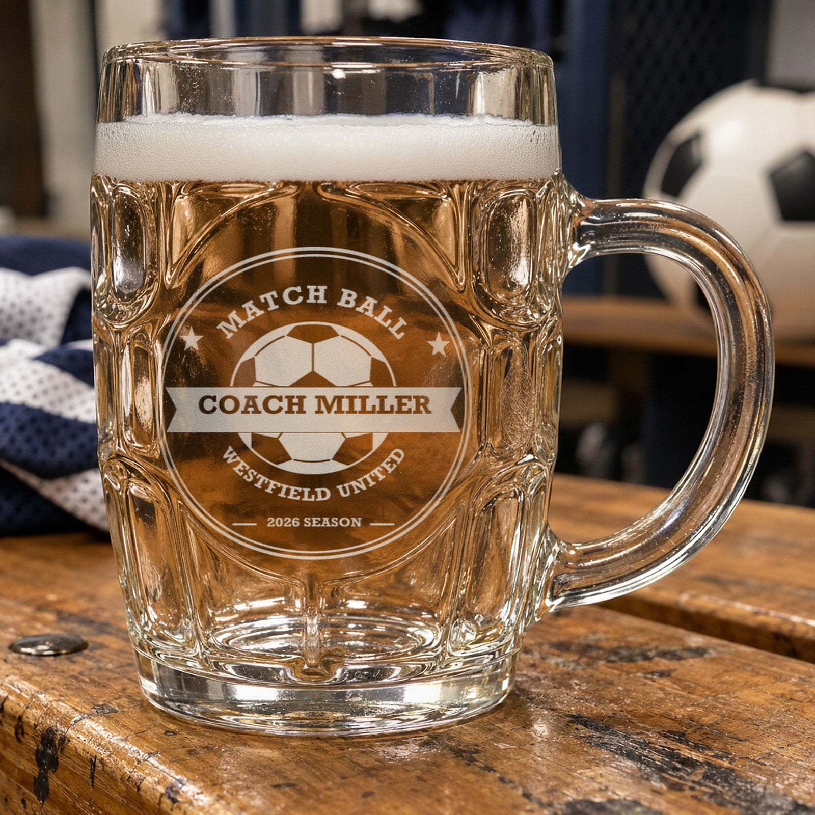 Personalized soccer coach beer stein on a locker room bench, frosted engraving reading Match Ball, Coach Miller, Westfield United and 2026 Season