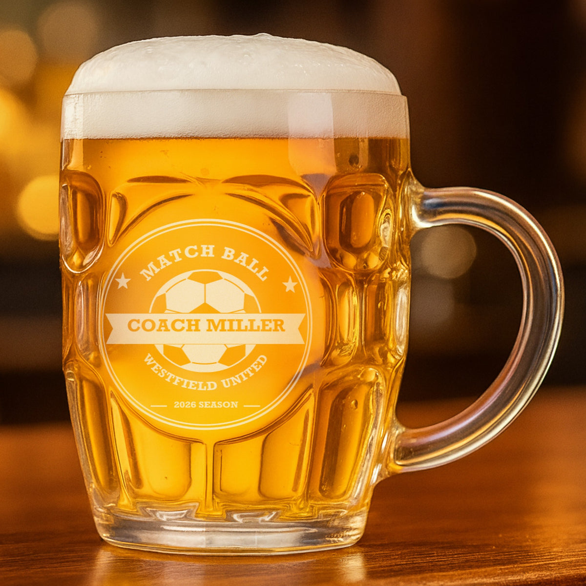 Match Ball soccer coach beer stein filled with golden lager on a bar, engraved with a soccer ball crest and Coach Miller across the center banner