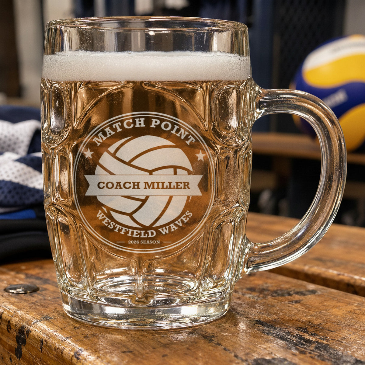 Personalized volleyball coach beer stein beside a volleyball and a pair of knee pads, frosted engraving reading Match Point, Coach Miller and Westfield Waves