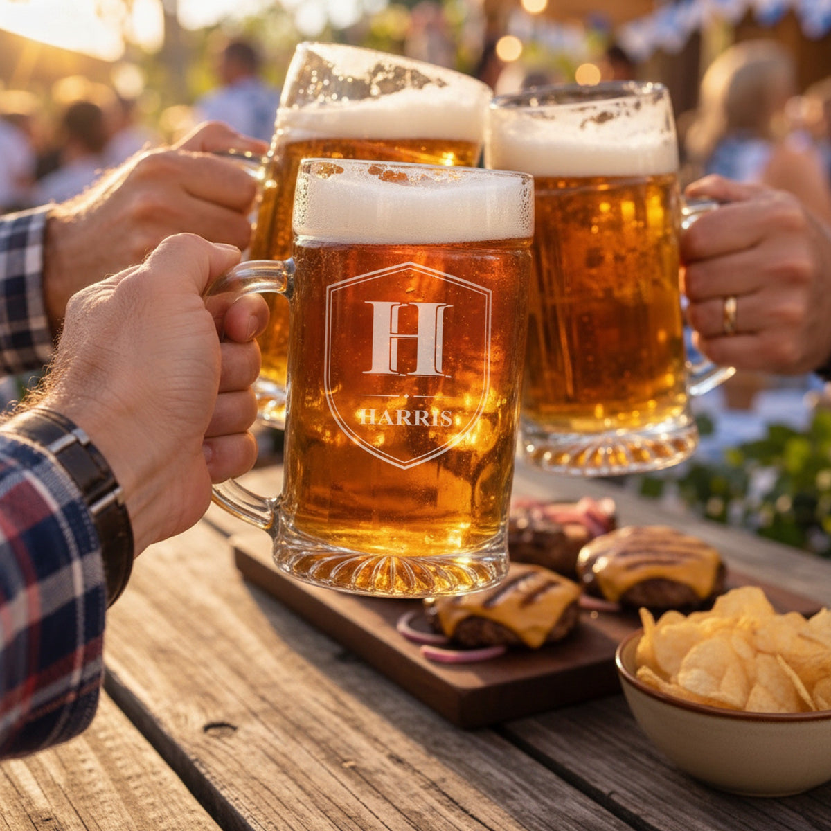 Three friends toasting with engraved 25 oz glass beer steins at a backyard cookout, the front stein etched with a Shield Crest reading H and Harris