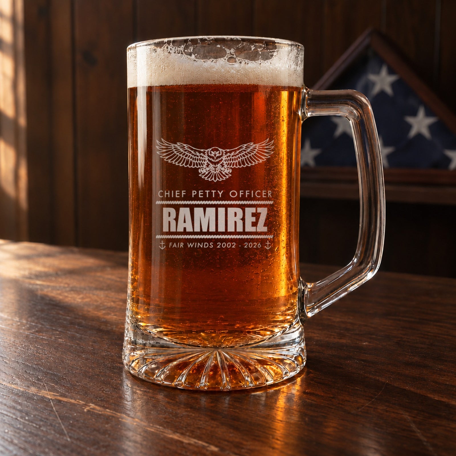 Navy retirement beer stein on a walnut desk with a folded flag case behind it, engraved with an eagle, Chief Petty Officer and Ramirez
