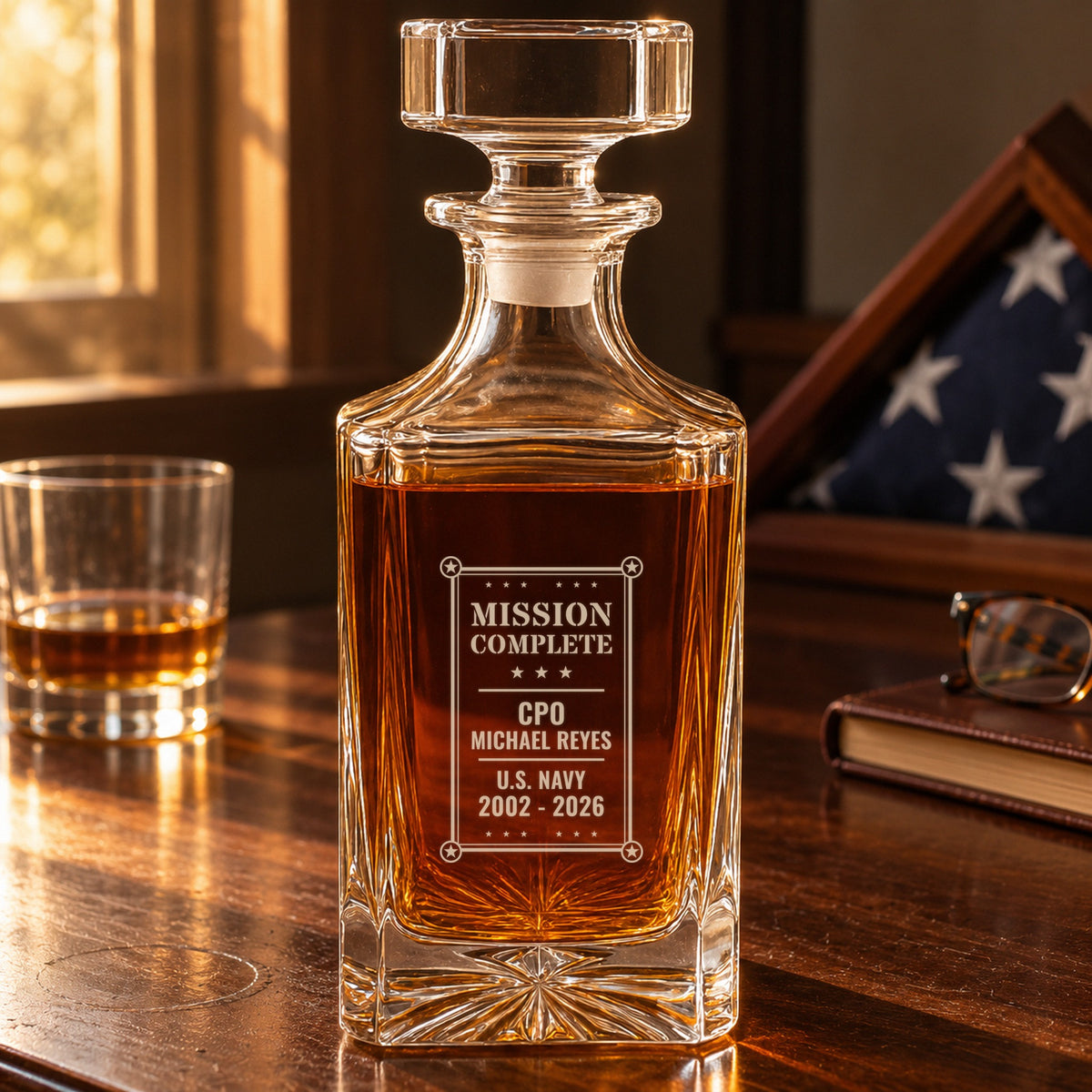Personalized retirement decanter engraved Mission Complete, CPO Michael Reyes, U.S. Navy, on a desk beside a folded flag case
