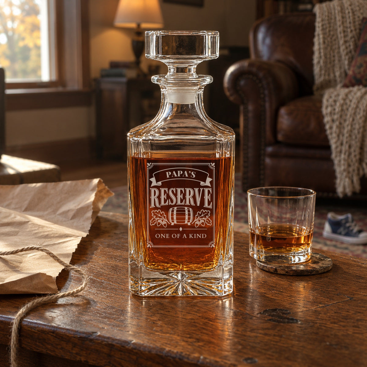 Engraved Papa's Reserve whiskey decanter on a living room coffee table beside torn kraft wrapping paper and a rocks glass, a personalized gift for grandpa