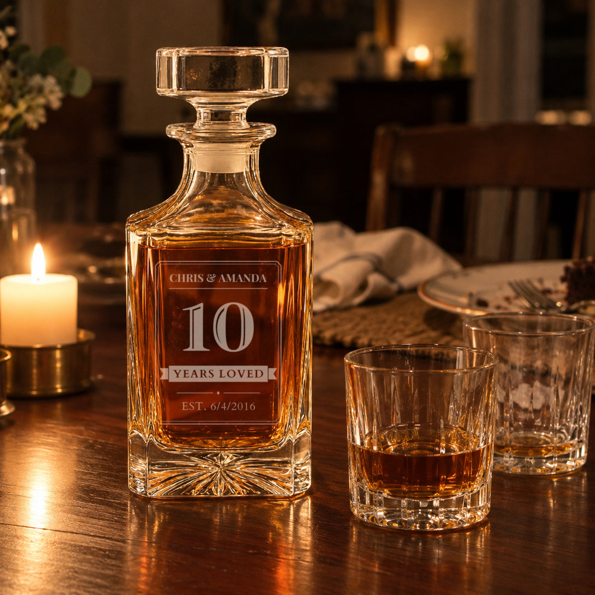 Personalized 10th anniversary decanter on a candlelit dinner table, engraved Chris and Amanda, 10, Years Loved, EST. 6/4/2016, beside two rocks glasses