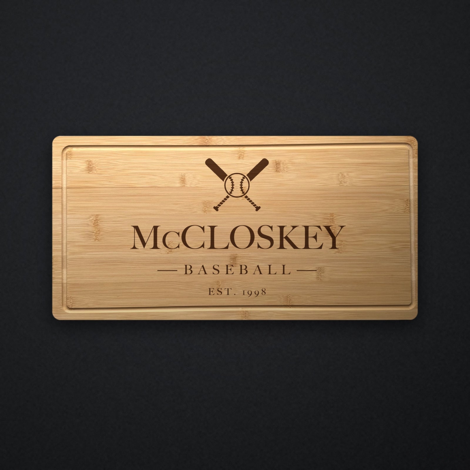 Personalized baseball coach cutting board in solid bamboo on dark slate, engraved with crossed bats and a ball above the name and the year.