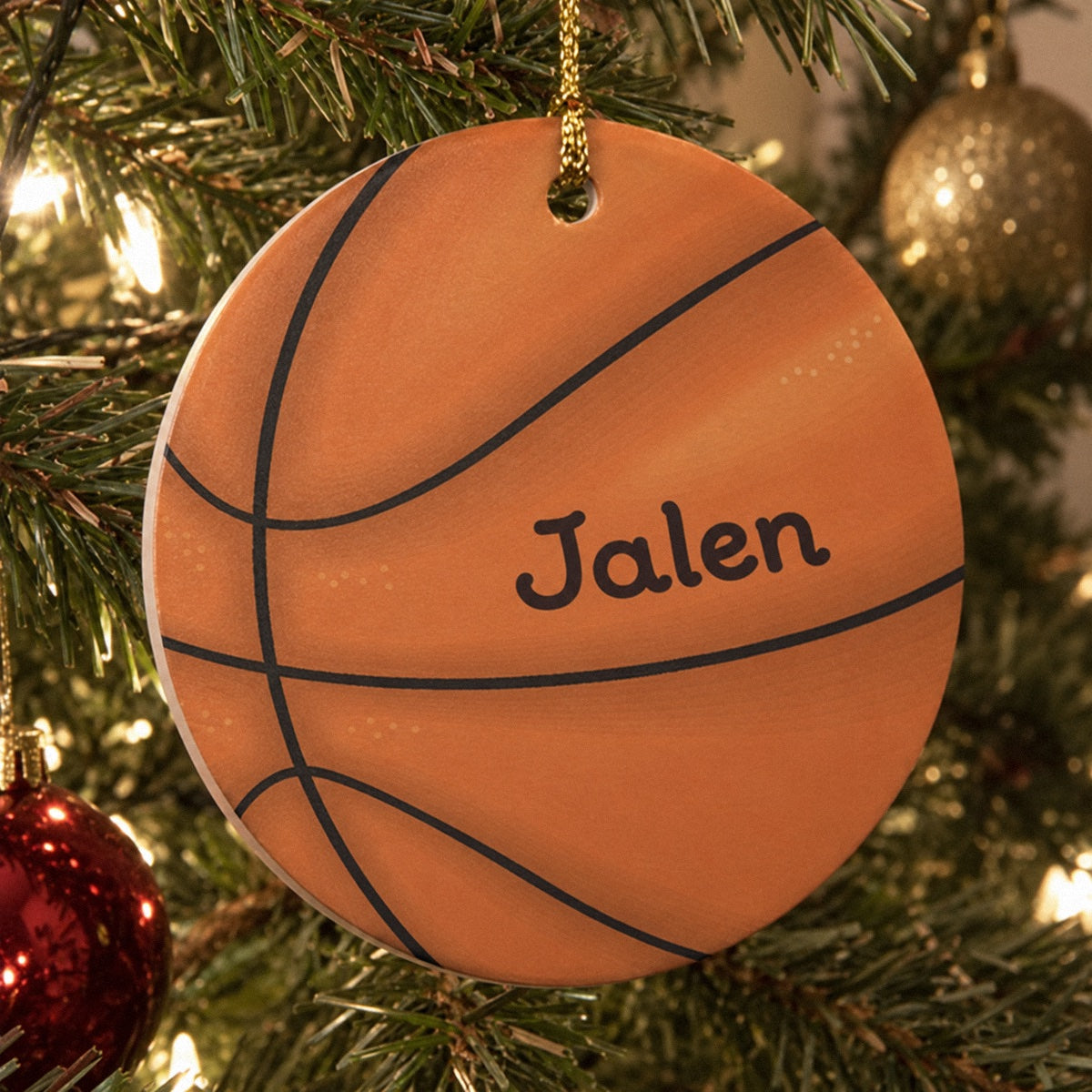 Personalized basketball ornament printed with the name Jalen hanging on a lit Christmas tree, a flat resin disc with a gold cord