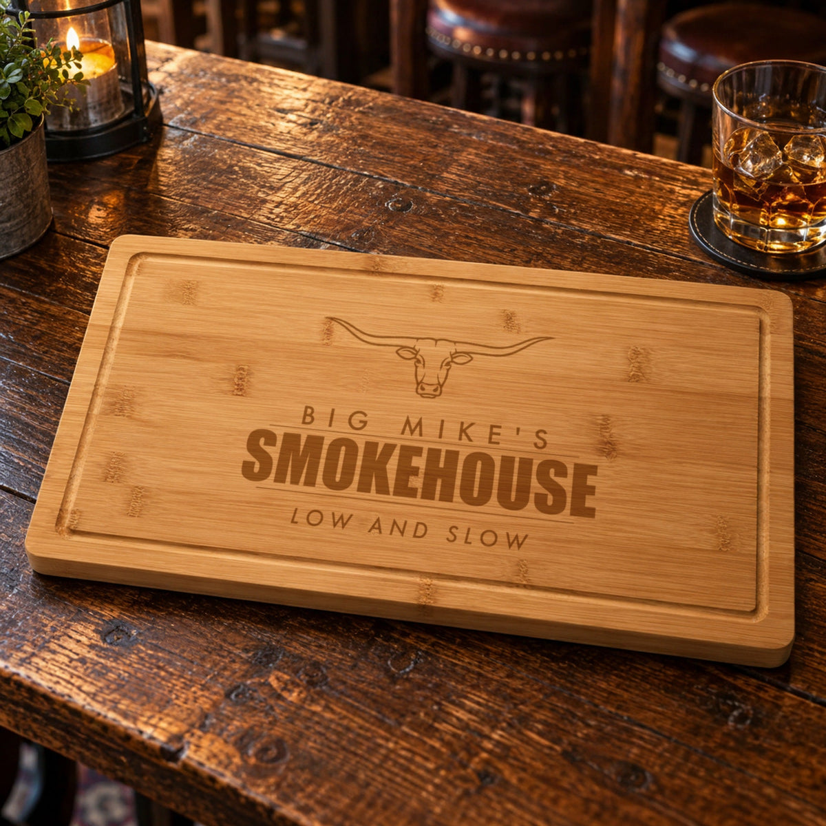 Bamboo cutting board on a tavern table engraved BIG MIKE'S SMOKEHOUSE LOW AND SLOW under a longhorn, a personalized gift for the guy who smokes meat