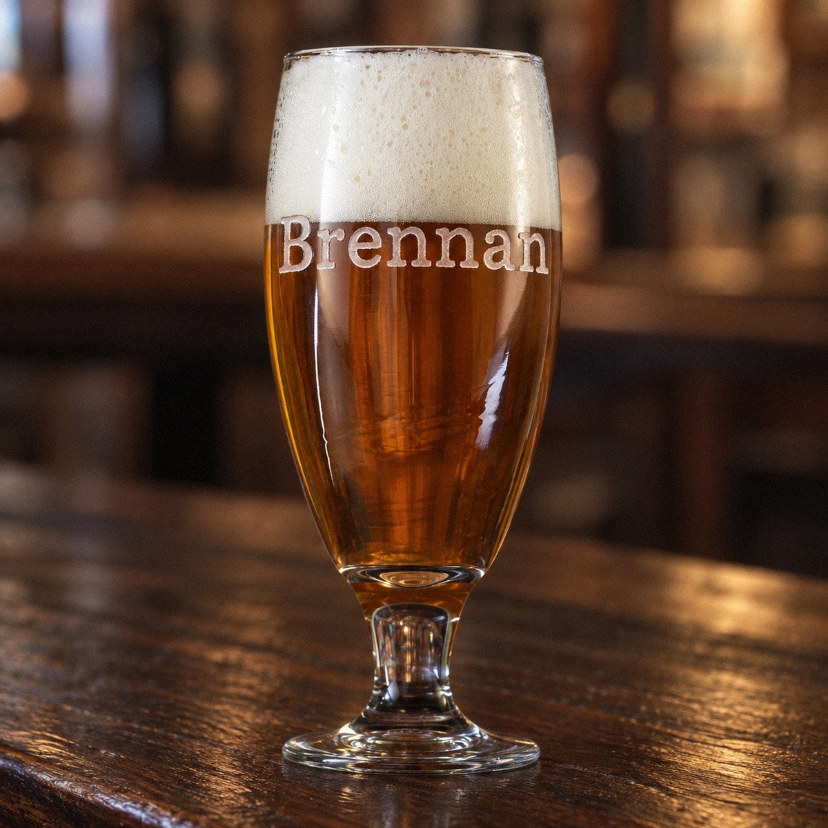 Personalized beer goblet full of amber ale on a walnut bar, sand-carved with the name Brennan in a large classic serif across the bowl