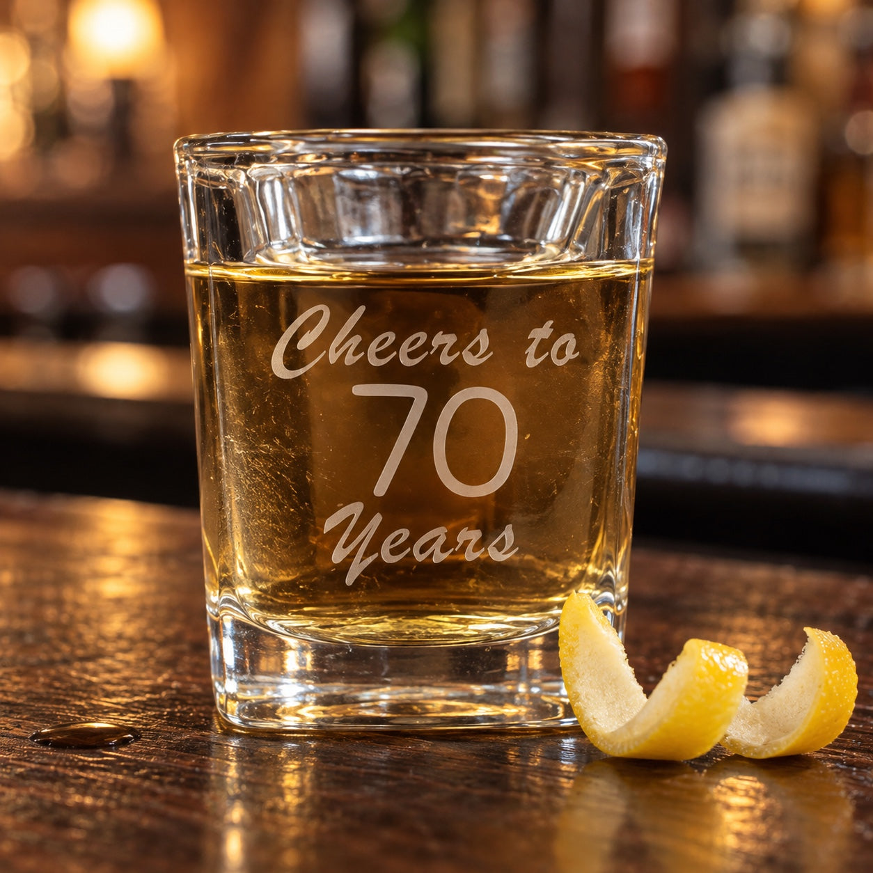 Personalized birthday shot glass etched Cheers to 70 Years, a shot of whiskey on a pub bar with a lemon twist, a birthday shot glass for him