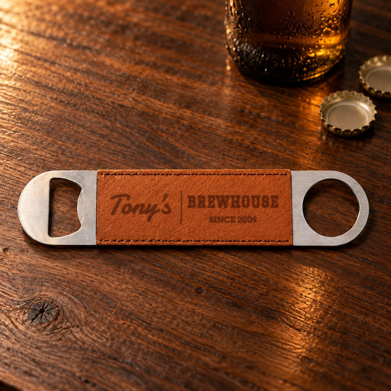 Personalized bottle opener from the beer mug gift set: tan faux leather sleeve burned with Tony's, Brewhouse and Since 2009 beside two bottle caps
