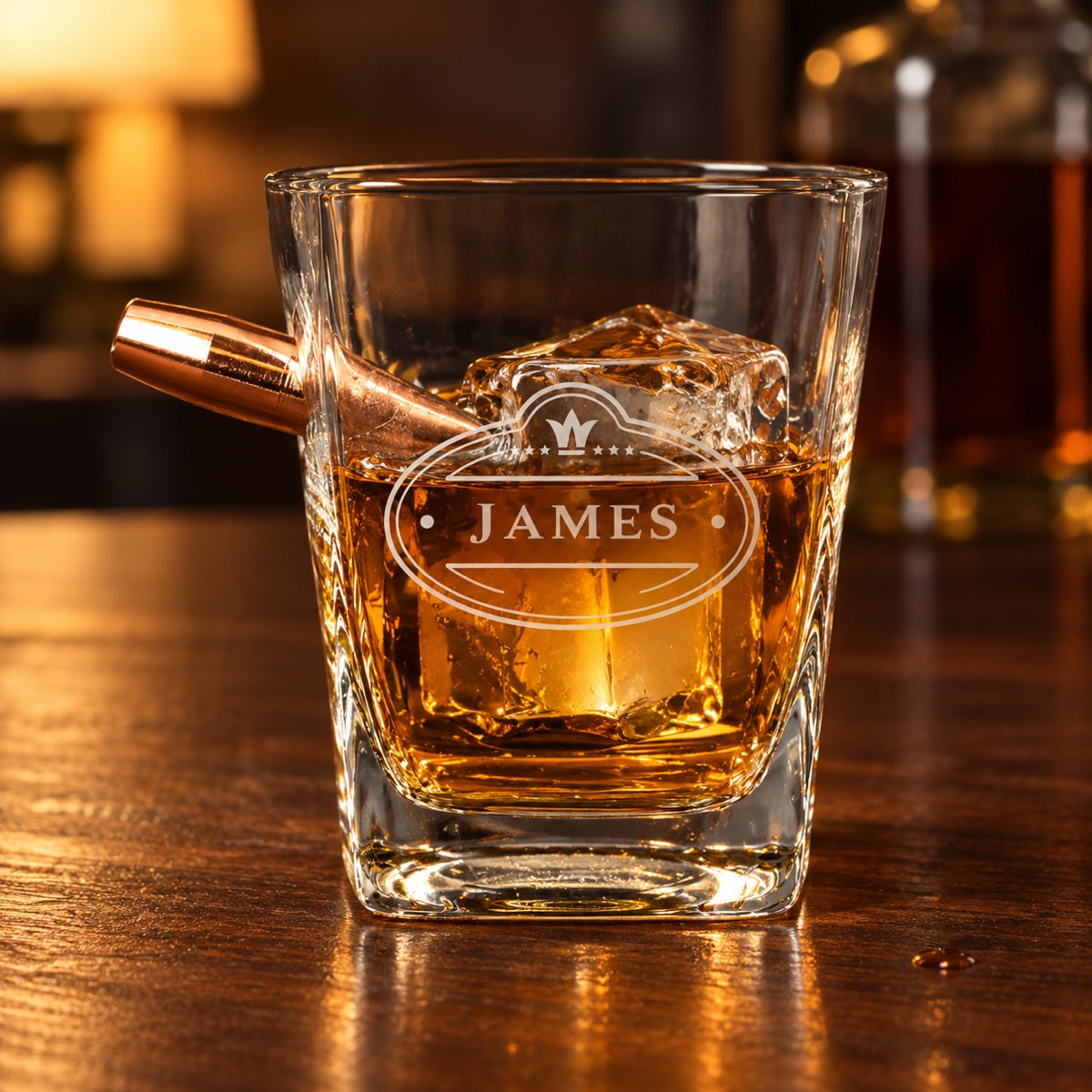 Personalized bullet whiskey glass with a faux .50 caliber bullet in the side and the name JAMES engraved in a crowned crest, bourbon on a walnut bar