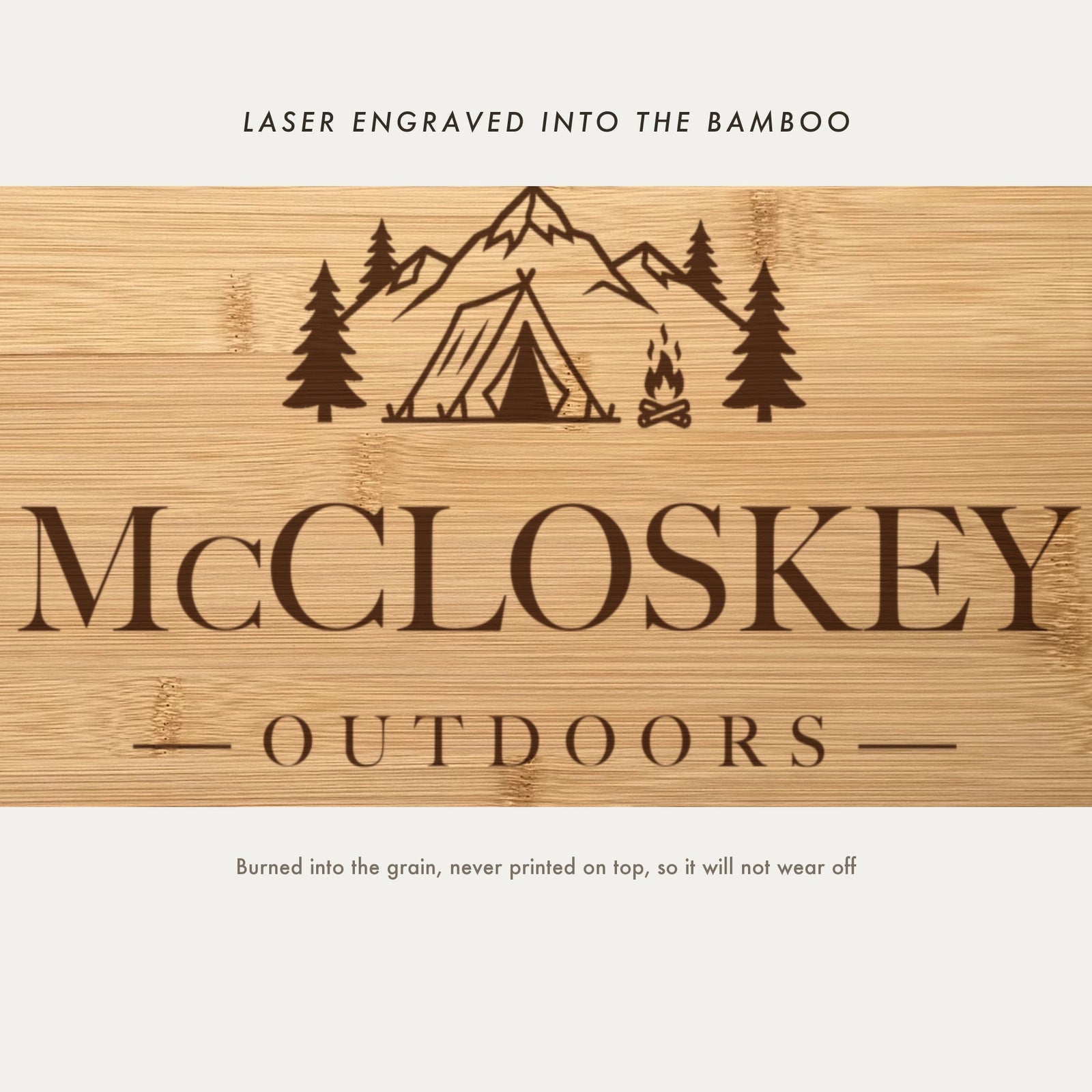 Close view of the tent, mountain range, pine trees and campfire laser engraved into the bamboo grain above the family name.