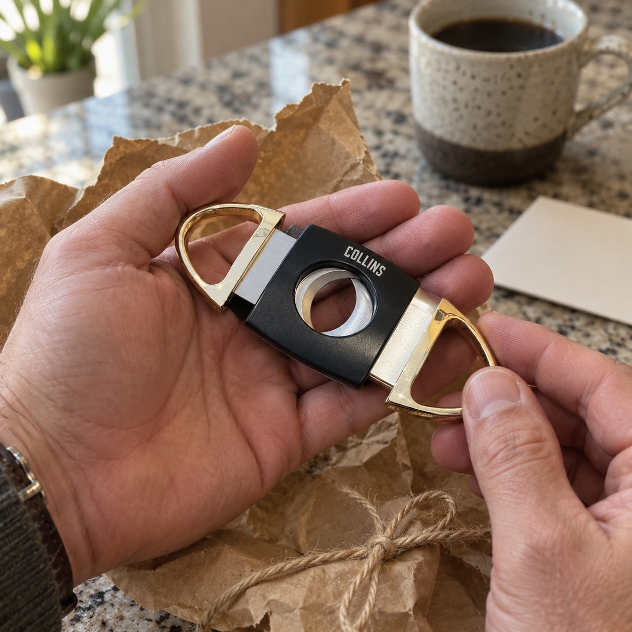 A man unwraps a personalized cigar cutter engraved COLLINS from brown kraft paper and twine at the kitchen island, a cup of coffee beside him.