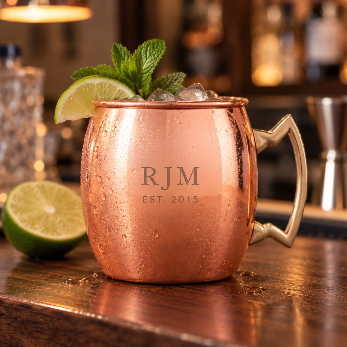 Personalized copper Moscow mule mug engraved with the initials RJM and EST. 2015, filled with a mule over ice with lime and mint on a walnut home bar.