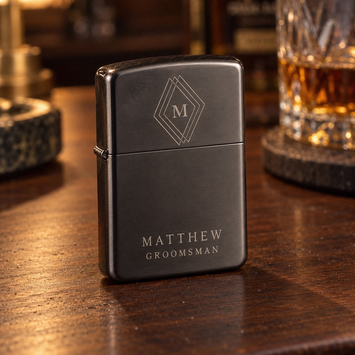 Personalized engraved flip-top lighter in gunmetal black with an M in a diamond and MATTHEW GROOMSMAN, standing on a walnut bar