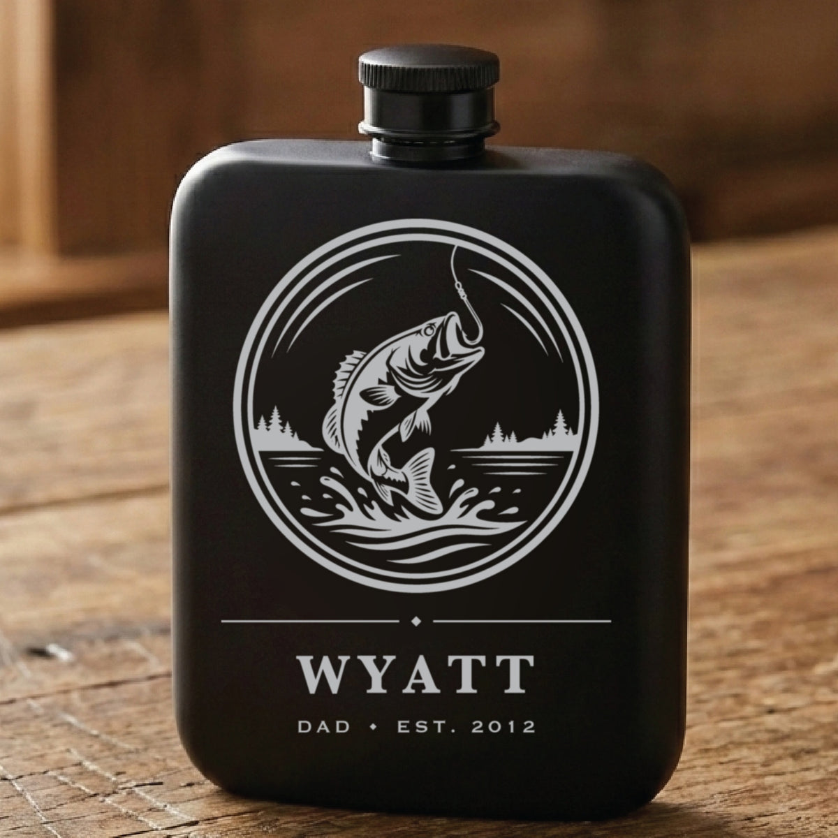Matte black personalized fishing flask laser engraved with a leaping bass above the name Wyatt, the word Dad and Est. 2012.