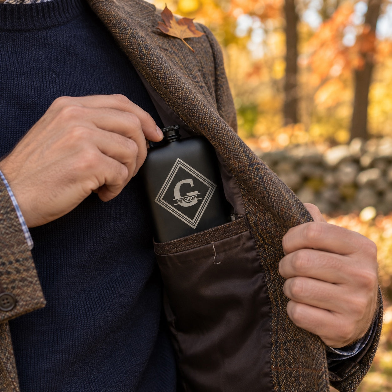 A man slips his personalized matte black flask with a George monogram into the inside pocket of his tweed jacket on a fall day