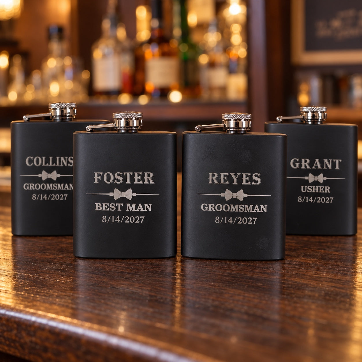 Four personalized flasks for groomsmen in matte black, engraved FOSTER Best Man, REYES and COLLINS Groomsman and GRANT Usher, each with a bow tie.