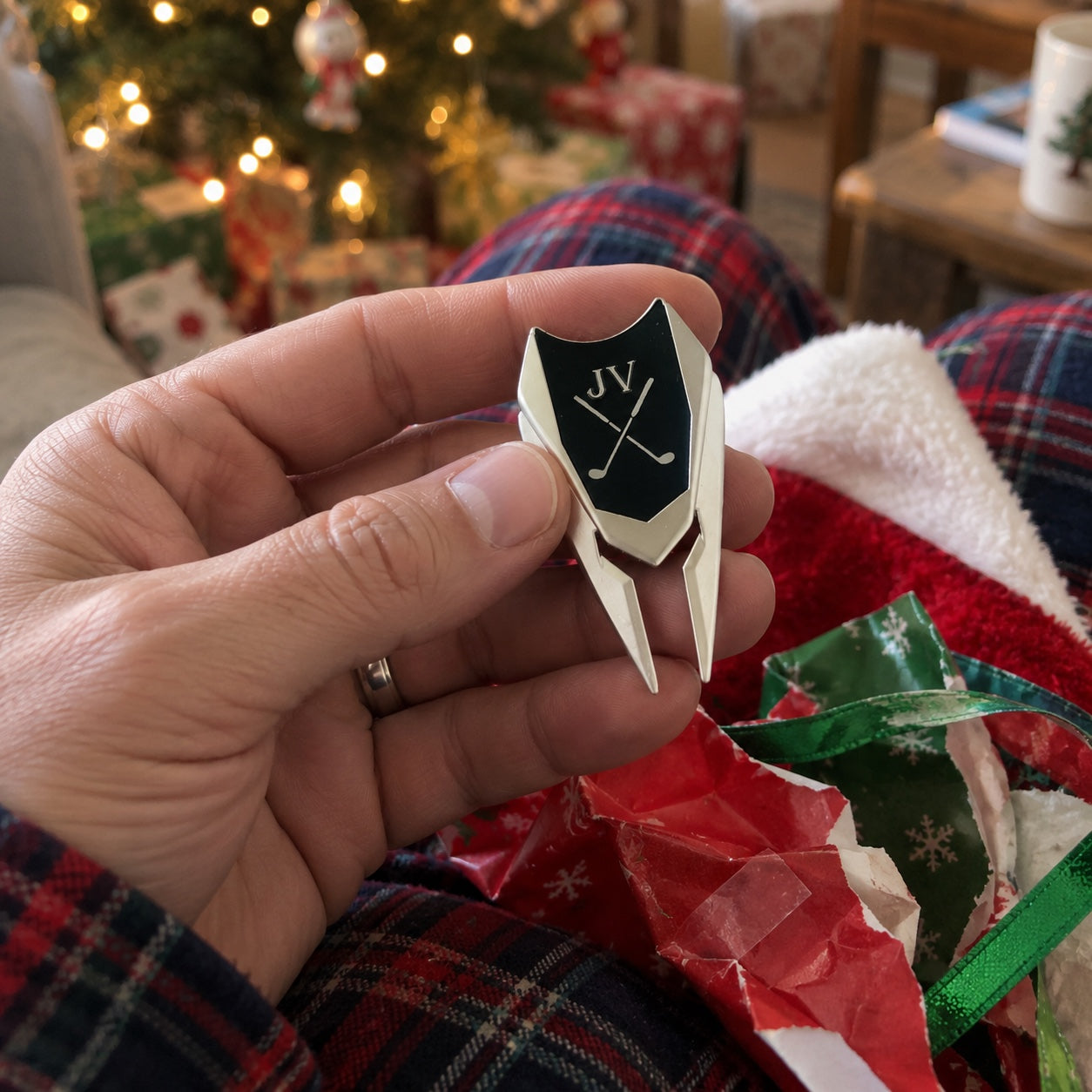 A man holds his personalized golf divot tool pulled from Christmas wrapping paper and a stocking, a small engraved golf gift for him