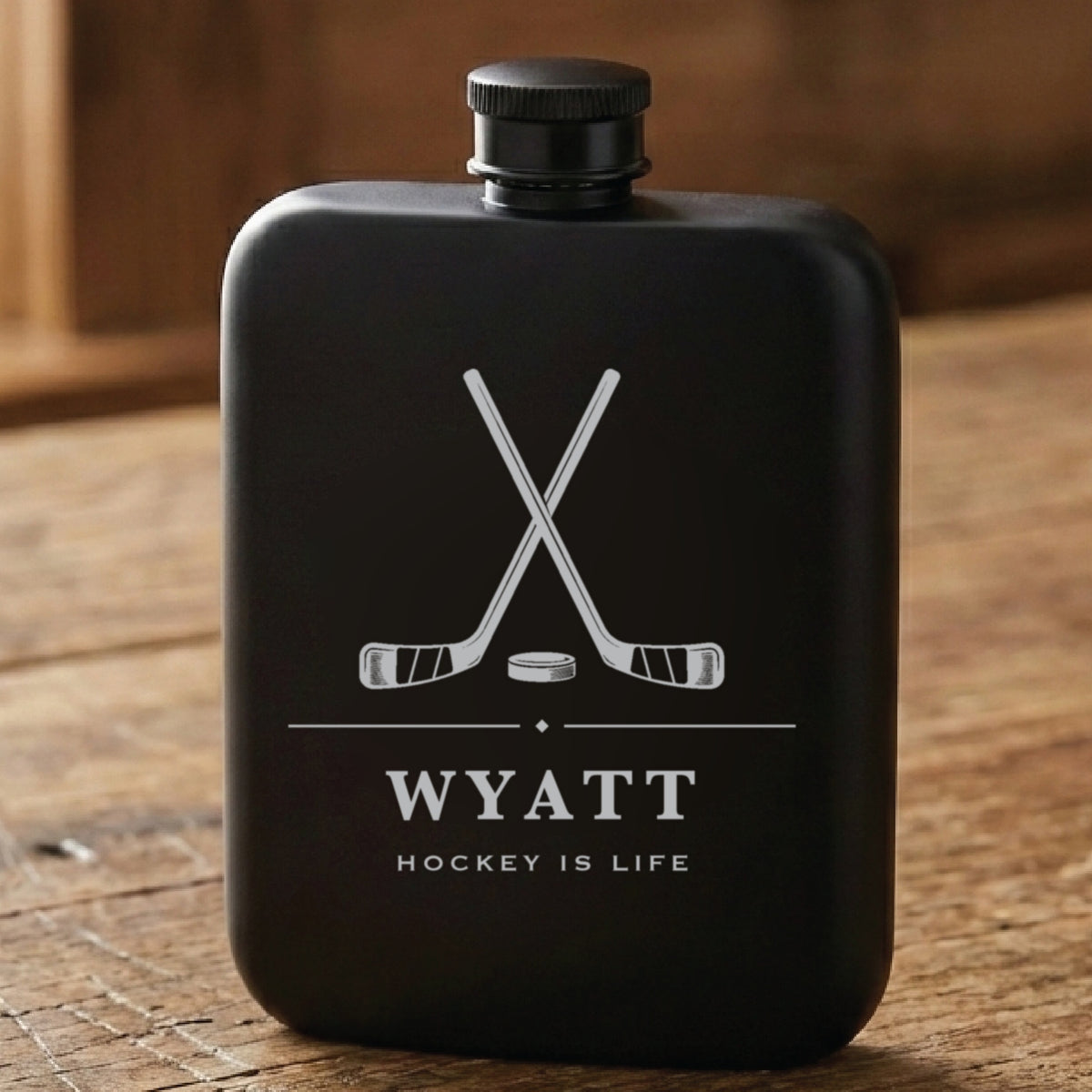 Matte black personalized hockey flask laser engraved with crossed sticks and a puck, the name Wyatt and Hockey Is Life.