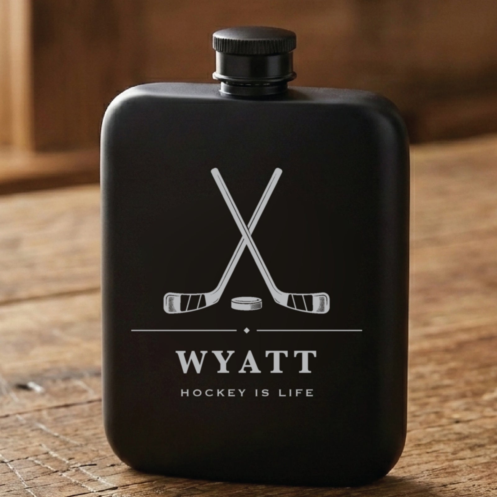 Matte black personalized hockey flask laser engraved with crossed sticks and a puck, the name Wyatt and Hockey Is Life.