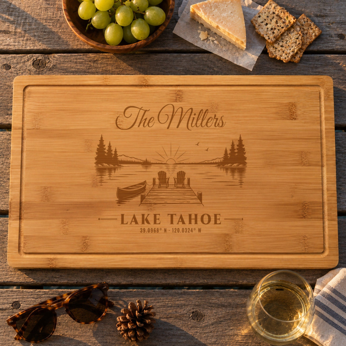 Personalized lake house cutting board engraved The Millers, Lake Tahoe and its coordinates over a dock at sunset, on lake dock boards with cheese and wine