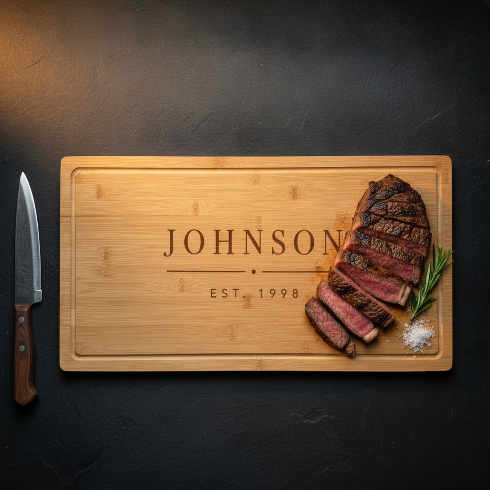 Large engraved bamboo carving board on dark slate with a sliced medium rare ribeye and rosemary, juices caught by the carved drip ring, carving knife alongside.