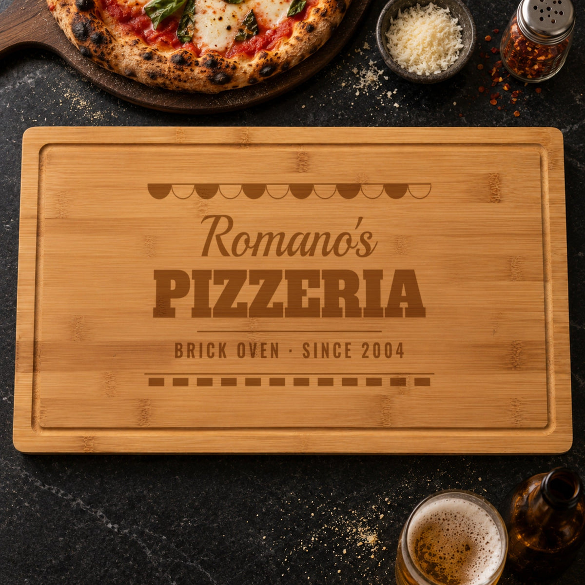 Personalized pizza cutting board engraved like a pizzeria sign, Romano's PIZZERIA BRICK OVEN SINCE 2004, beside a margherita pizza and parmesan