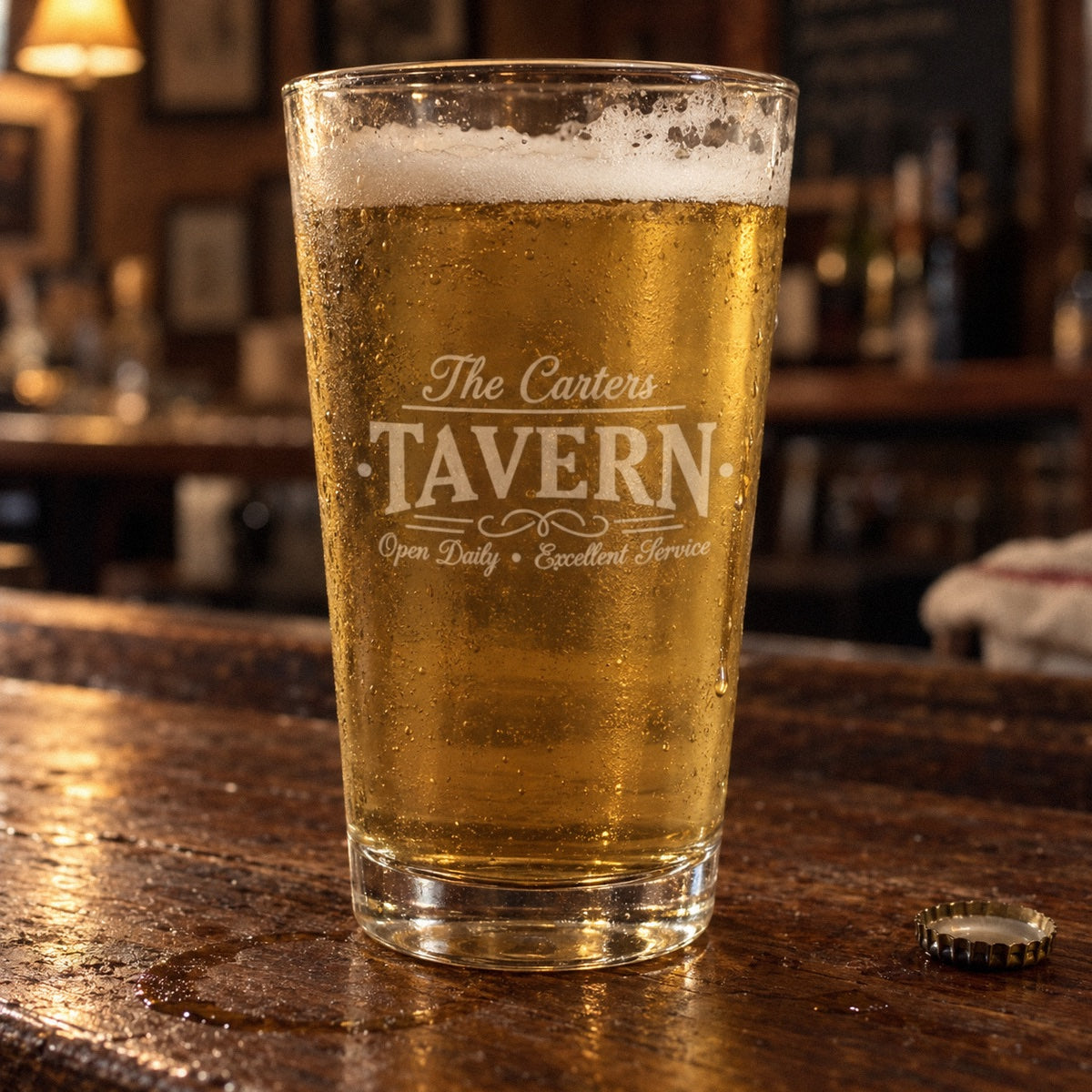Personalized tavern pint glass etched The Carters above TAVERN and Open Daily, Excellent Service, filled with lager on a home bar