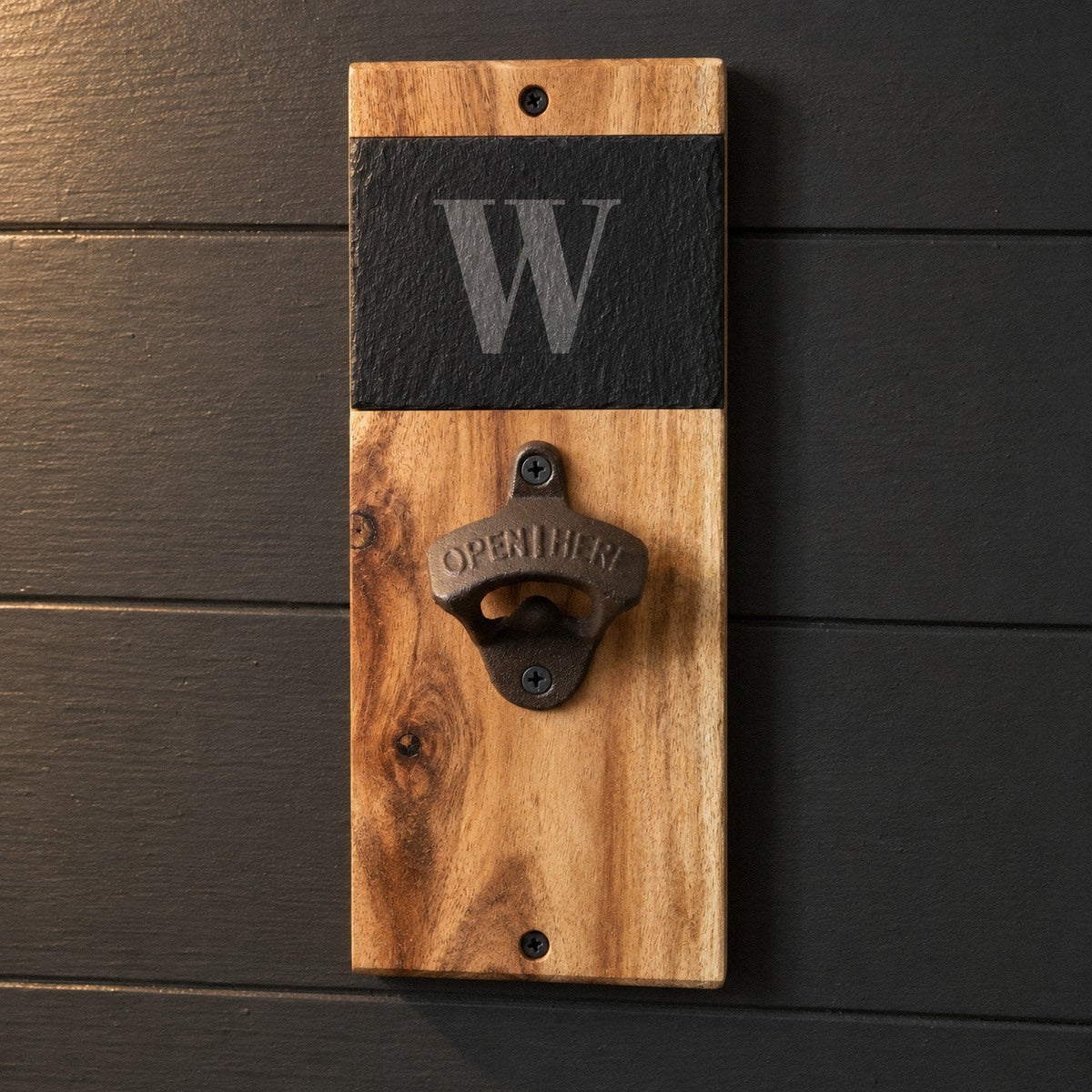 Personalized wall mounted bottle opener in acacia wood and slate on a charcoal wall, the slate engraved with a bold W above the iron opener