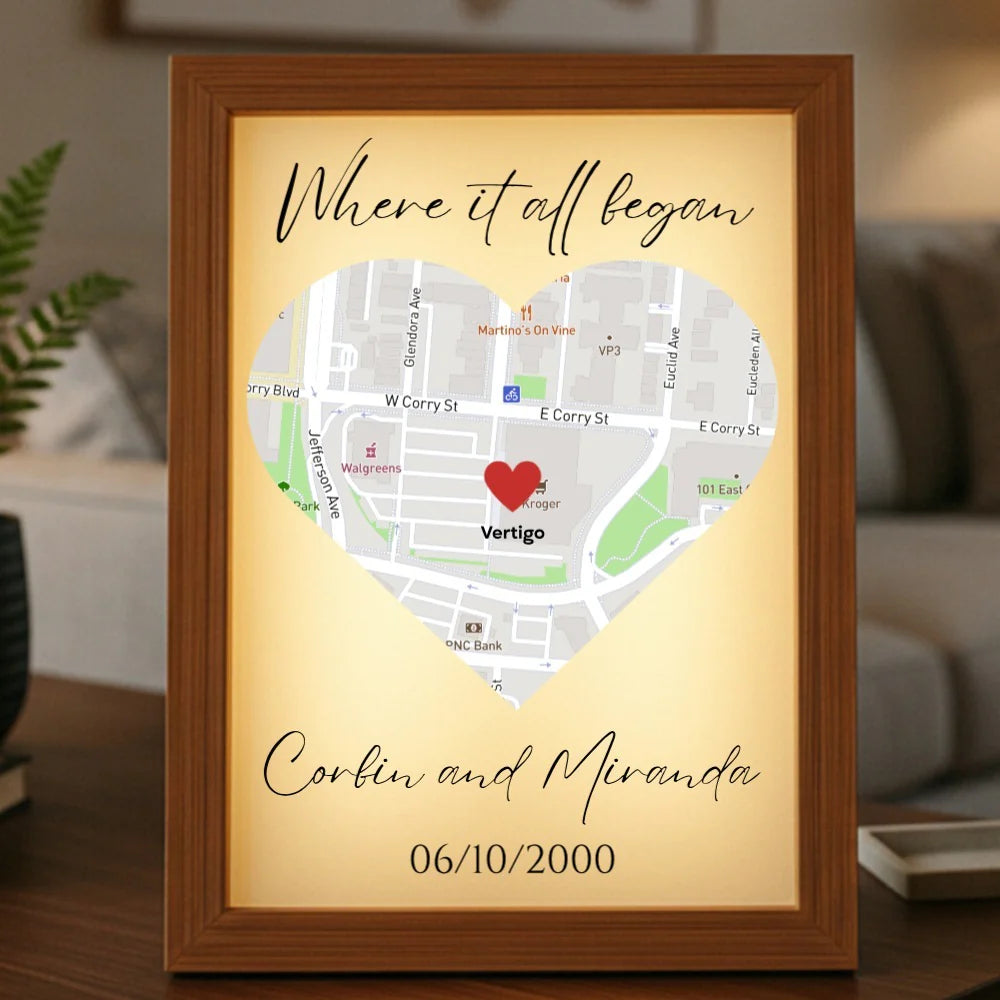 Framed personalized map art with heart marker on sample location, inscribed "Where it all began" with names "Corbin and Miranda" and date "06/10/2000" on cream background in wood frame