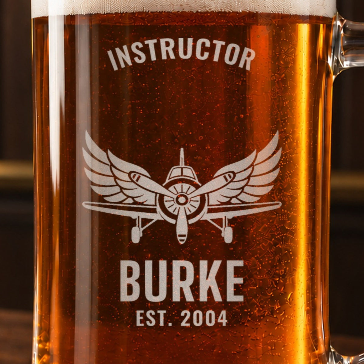 Close-up of the frosted engraving on the pilot beer stein, a vintage propeller airplane and spread wings: Instructor, Burke, Est. 2004