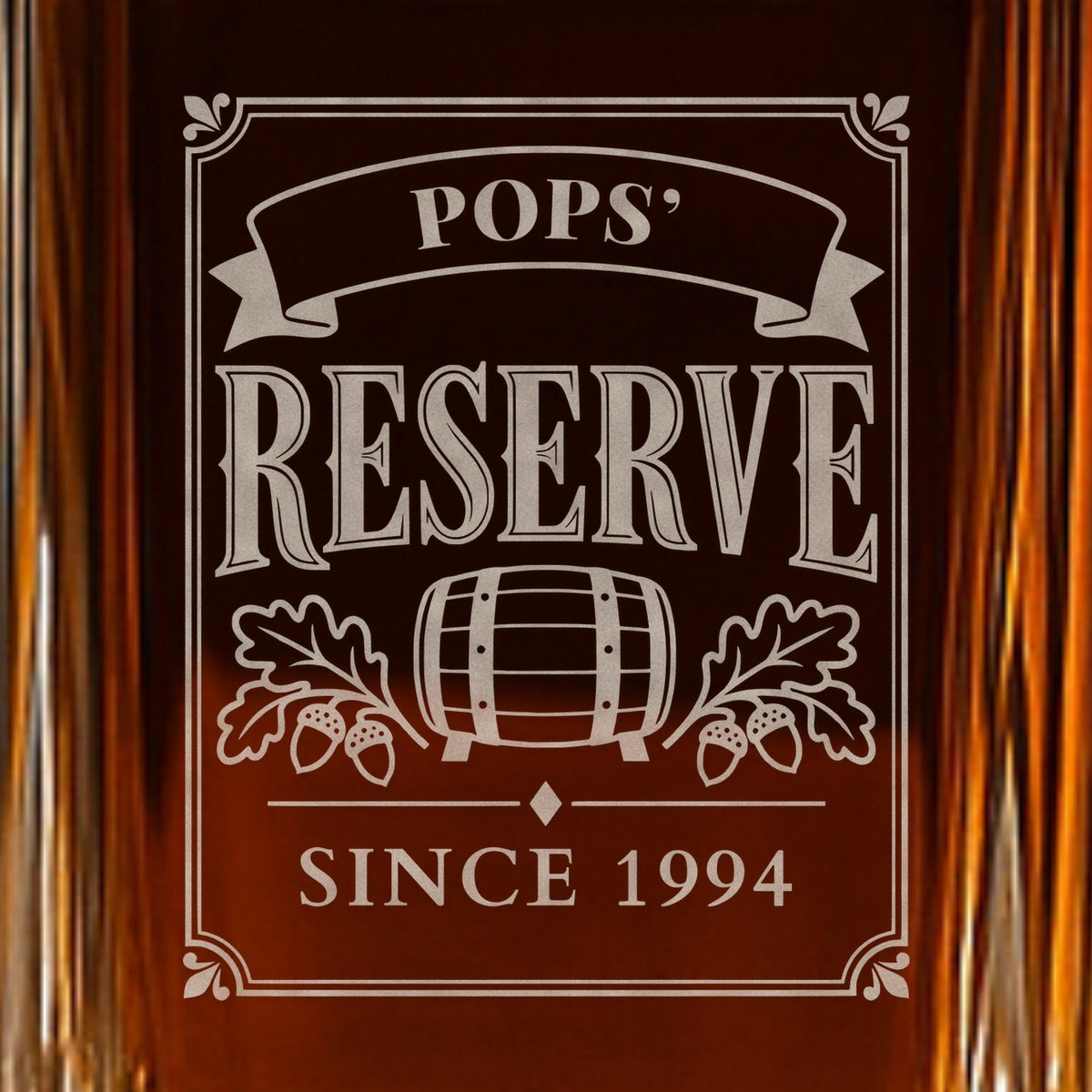 Close-up of the frosted Pops' Reserve label engraved on a whiskey decanter: a ribbon, barrel and oak leaves over the line Since 1994