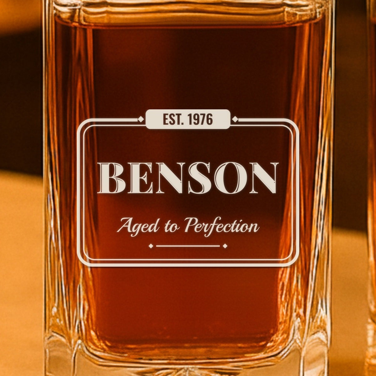 Close-up of the frosted laser engraving on the birthday decanter: EST. 1976 in the tab, Benson in vintage capitals and Aged to Perfection in script