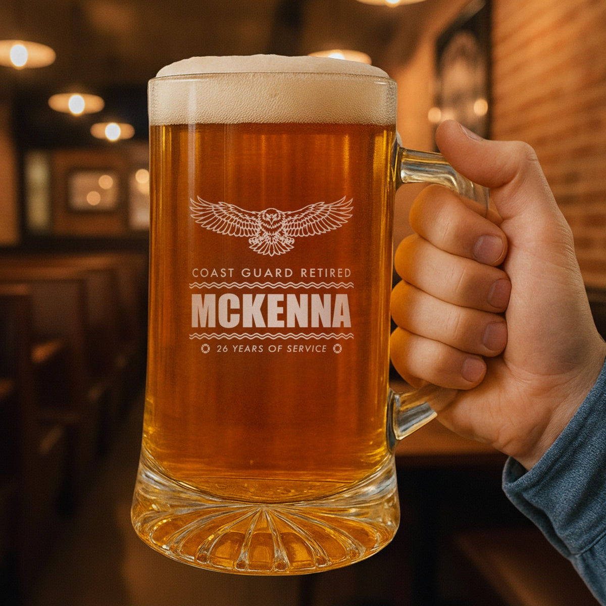 Hand holding a 25 oz personalized Coast Guard retirement beer stein in a pub, engraved Coast Guard Retired, McKenna and 26 Years of Service