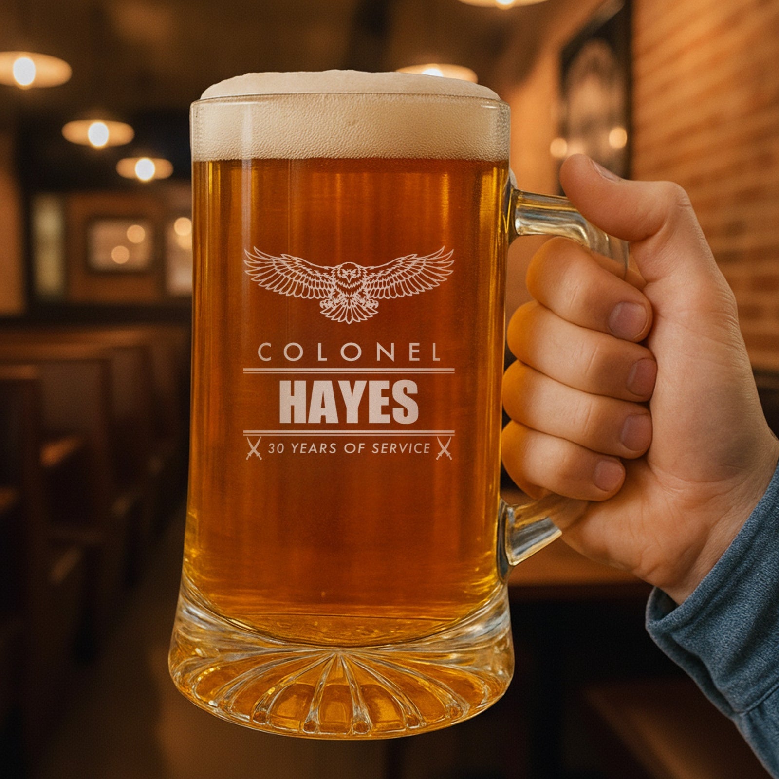 Hand holding a 25 oz personalized Marine retirement beer stein in a pub, engraved with an eagle, Colonel, Hayes and 30 Years of Service