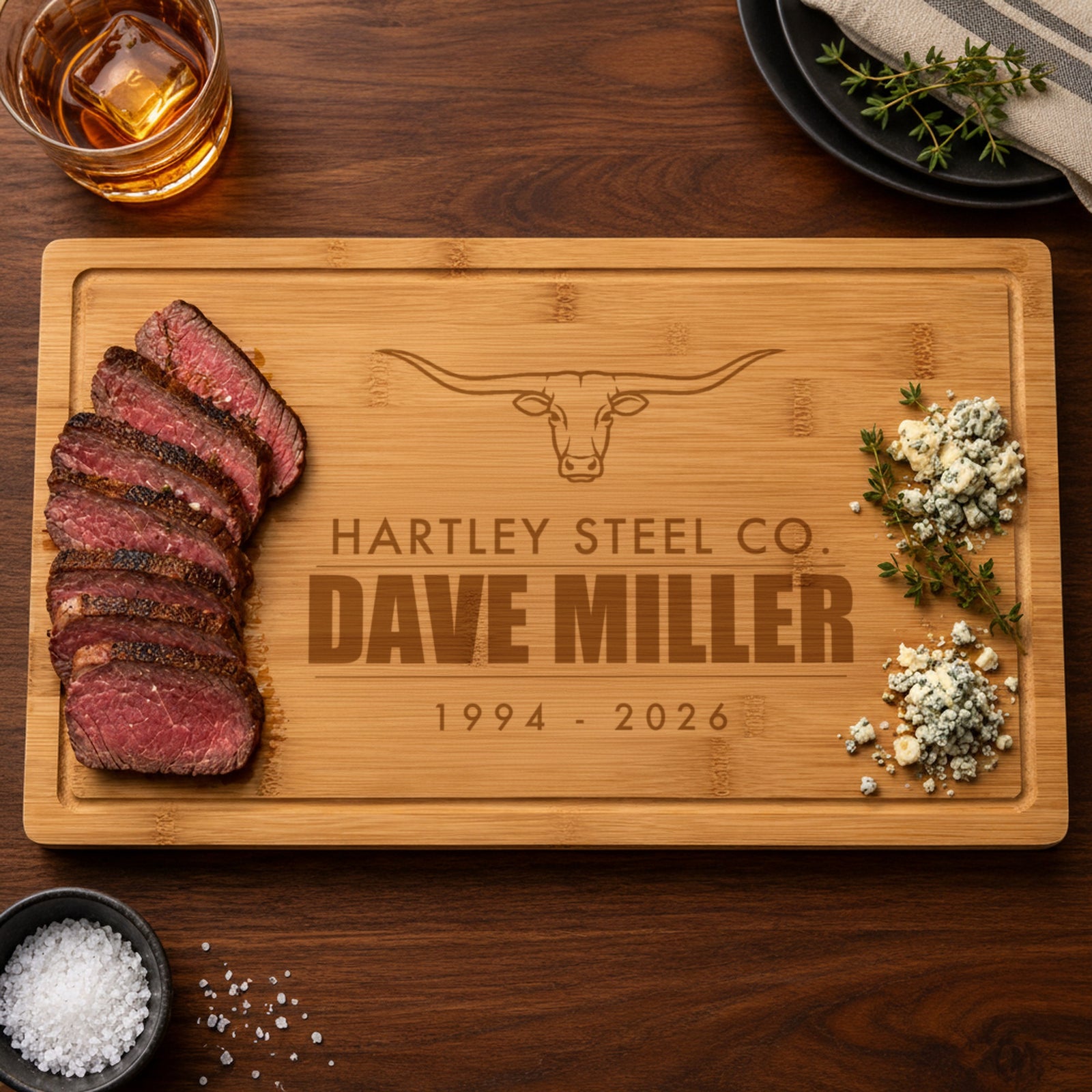 Personalized retirement cutting board engraved with a longhorn steer, Hartley Steel Co., Dave Miller and 1994 - 2026, set with sliced steak and herbs
