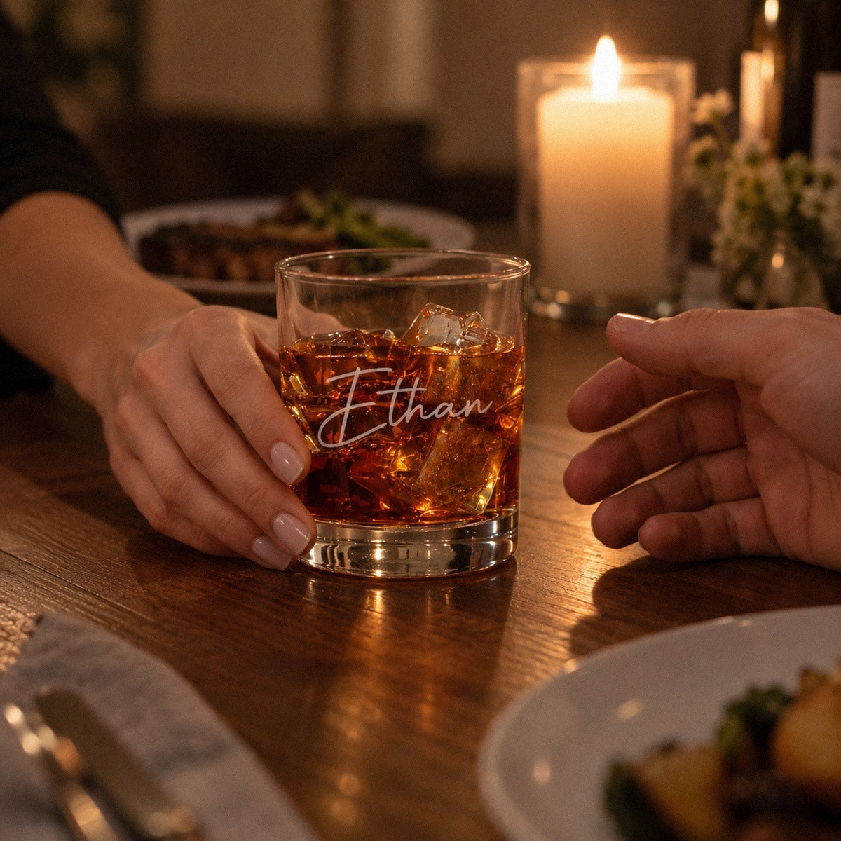 A woman slides a whiskey glass engraved Ethan across a candlelit dinner table, a romantic gift for him with my heart on the back