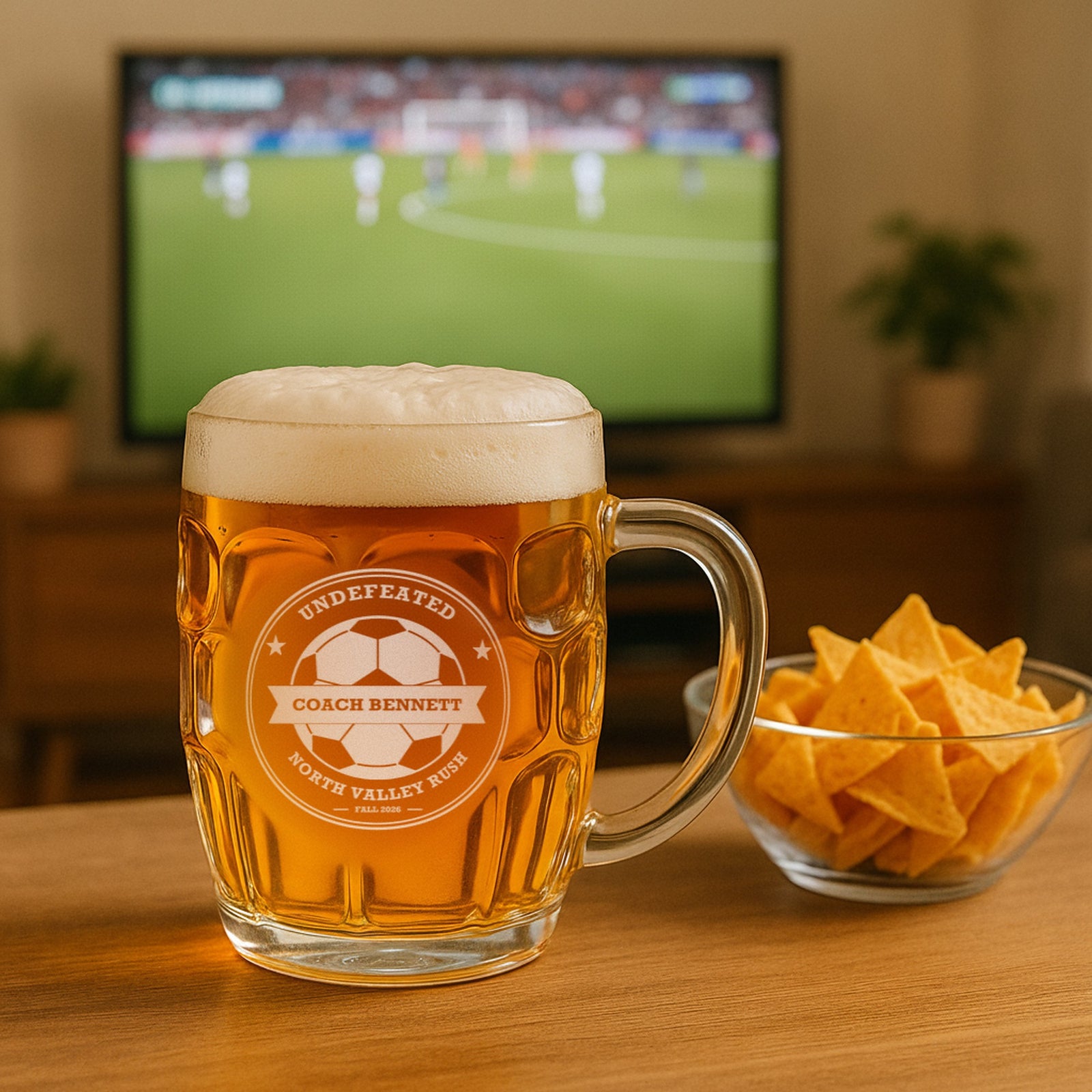 Soccer coach beer mug engraved Undefeated for Coach Bennett of North Valley Rush, on a table with a soccer match on TV