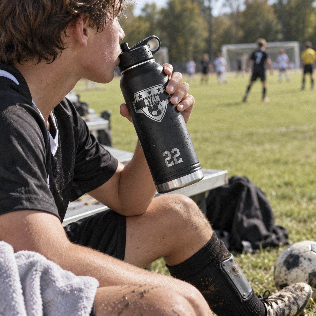 A soccer player drinks from a personalized water bottle engraved RYAN and 22 on the sideline bench during a game, a gift for soccer players