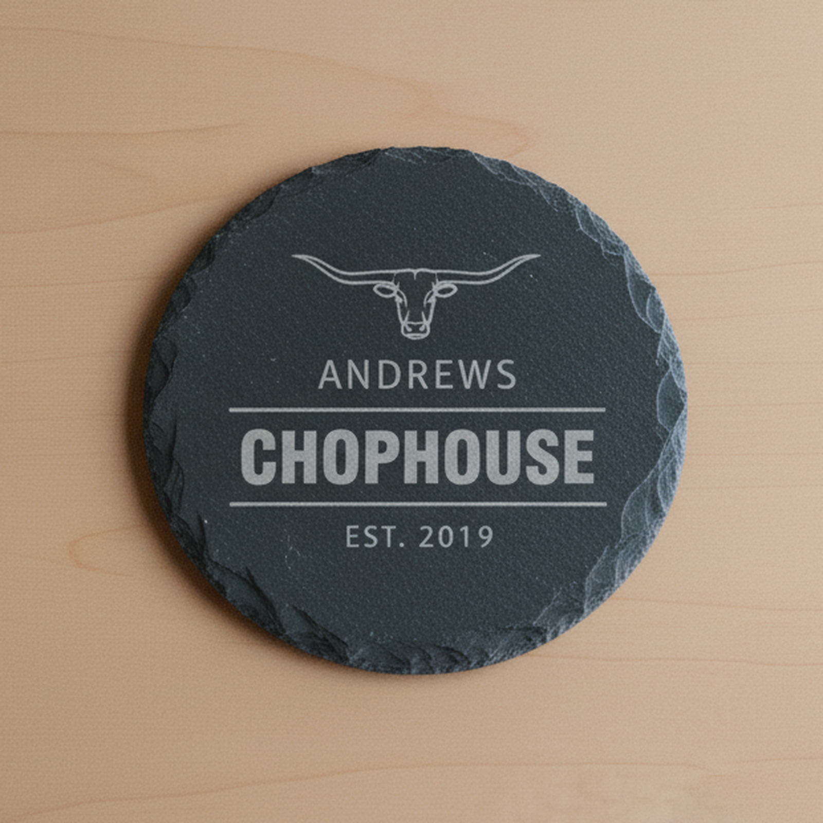Close detail of a single personalized steakhouse slate coaster showing the longhorn emblem engraving and natural slate texture
