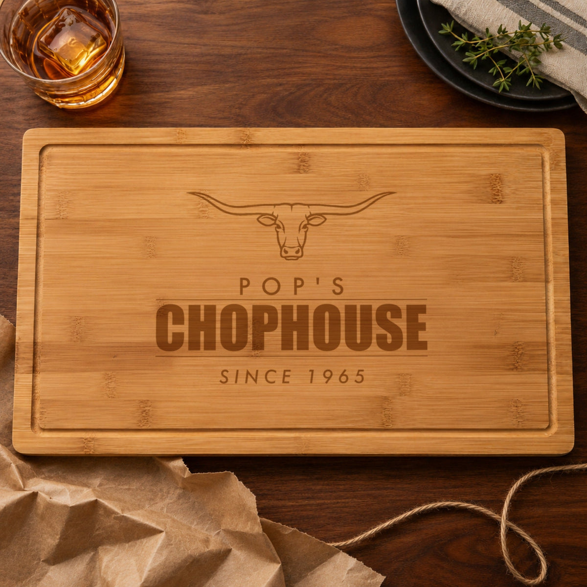 Personalized cutting board gift for dad engraved POP'S CHOPHOUSE SINCE 1965, just unwrapped from brown kraft paper on a walnut table
